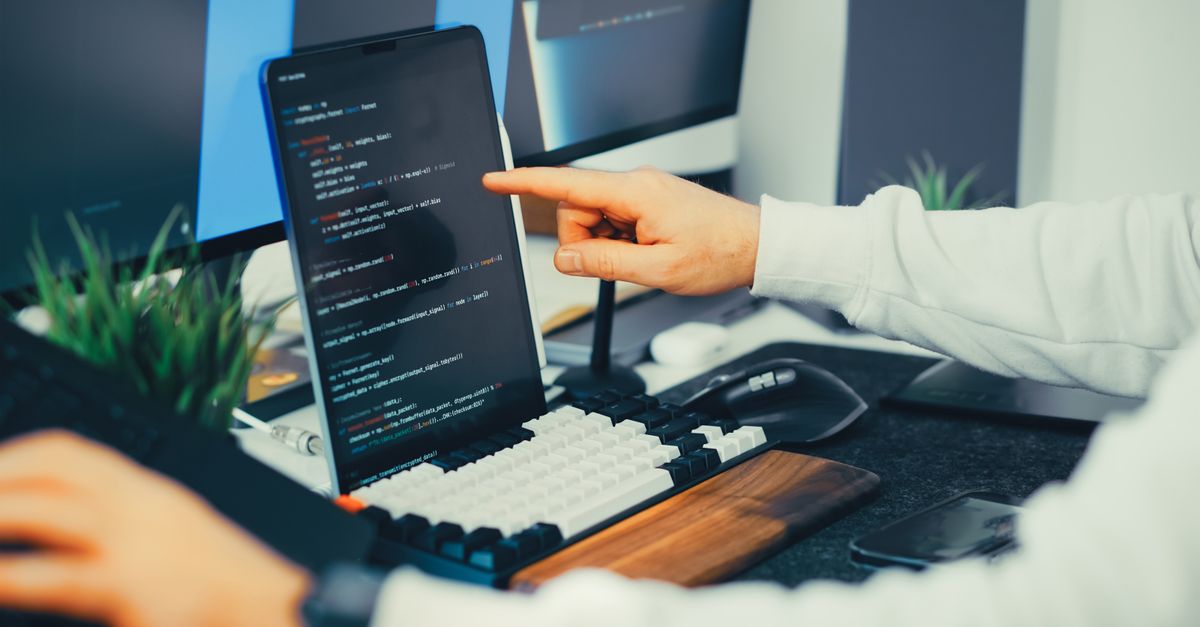 Two developers reviewing a content spreadsheet on dual monitors.